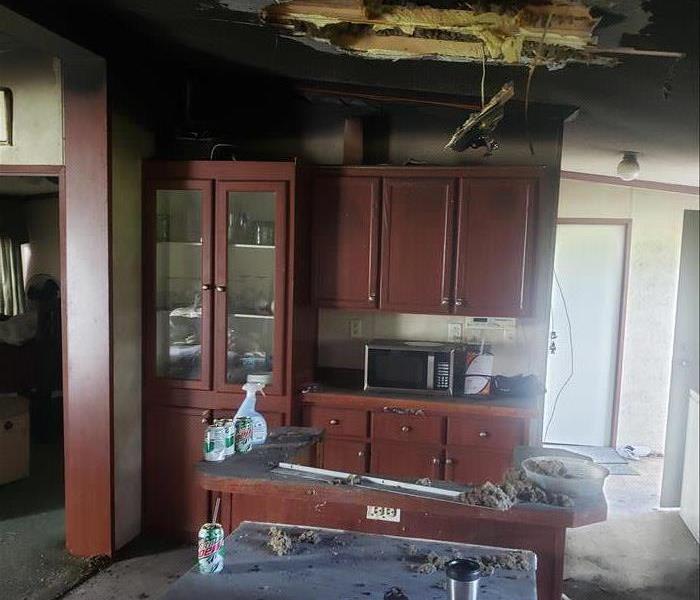 kitchen area that had been damaged by a fire. soot and debris cover the floor, kitchen island and big hole in the ceiling