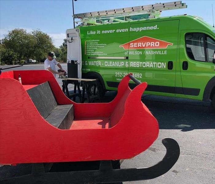 Red Santa sleigh is positioned in front of a Servpro van. A Servpro employee is cutting wood that will be used on the sleigh