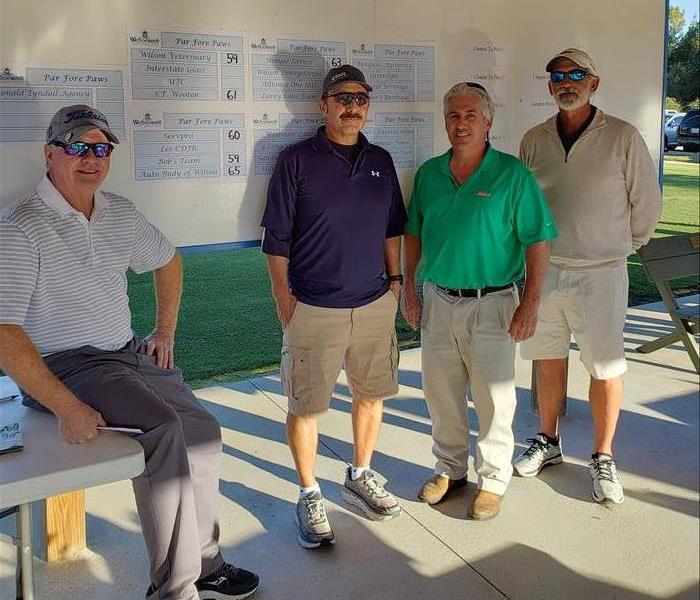 Franchise owner stands with 3 other teammates in front of score chart at golf course