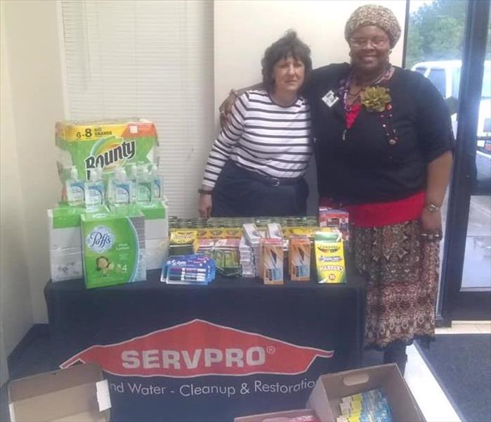 Co-Owner stands with a teacher beside table of donated school supplies