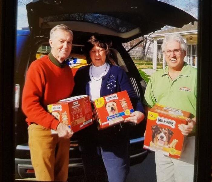 franchise owners pose with owner of dog shelter, showing dog treats and food for donation