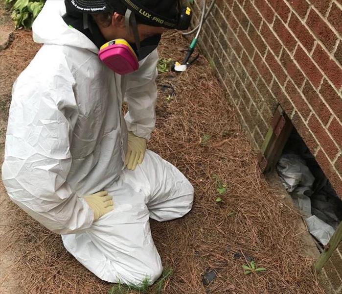 SERVPRO technician wearing personal protective equipment, kneeling in front of crawlspace